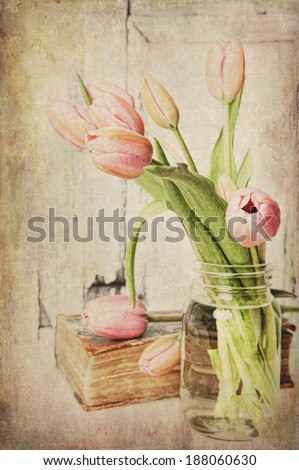 Fine art image of pink tulips in a jar next to a vintage book. Textured.