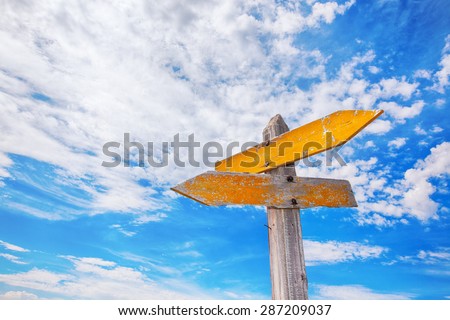 Rustic yellow crossroads sign against a cloudy blue sky.