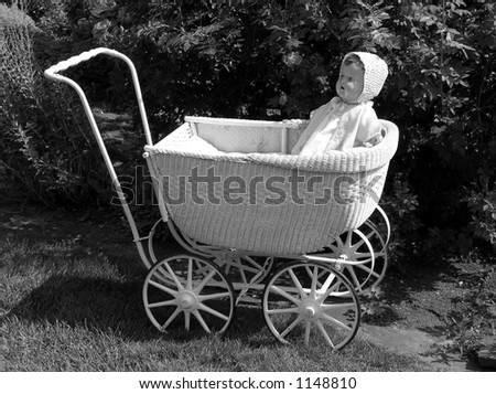 Antique doll & carriage in front of old-fashioned rose bush. Vintage garden.