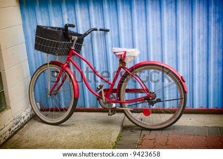 Old, 1950\'s era, red bike leaning against a blue wall.
