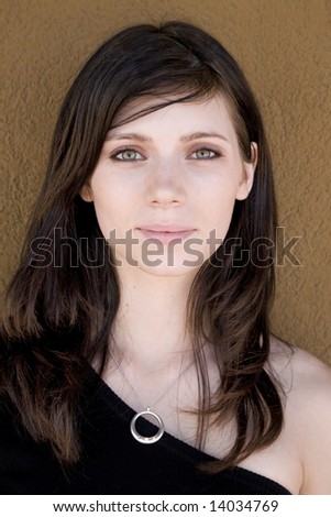 Portrait of a beautiful woman with gorgeous green eyes against a neutral earth tone colored wall.