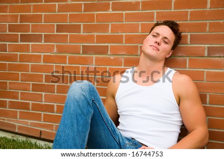 A young man leaning against a brick wall quietly thinking & reflecting on the past & the future.