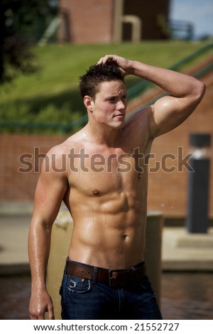 A young bare chested man cooling off in the water, on a hot summer day.