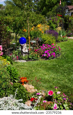 A beautiful, curving flower bed full of blooming annuals & perennials, line a sunny backyard.