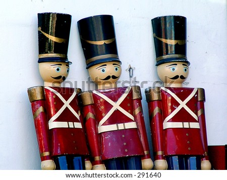 three tall wooden soldiers with red coats and top hats leaning up against a concrete wall