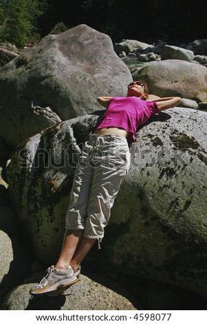 Woman resting in the sun on large rocks by a river