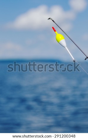 Vibrant End Of Fishing Rod With Bobber In Lake. Vertical image of the end of a fishing rod with a bobber out on a lake. Has plenty of copy space.