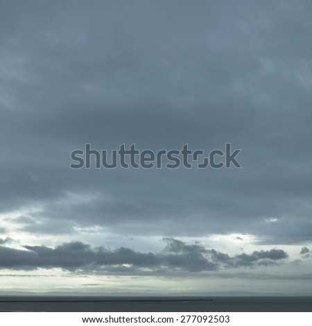 Gray ocean water with a silhoutted spit of land with a huge sky above