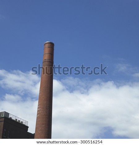 Tall brick smoke stack and factory wall against a blue sky