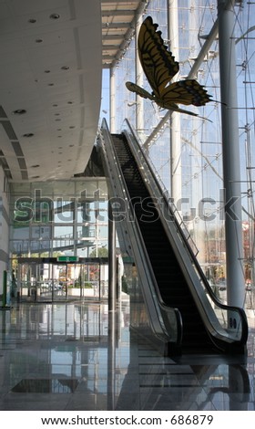 Building interior showing escalator and glass walls with butterfly sculpture hanging from the ceiling