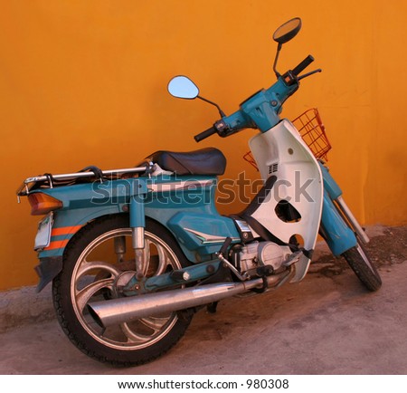Blue motorbike parked by a bright orange wall