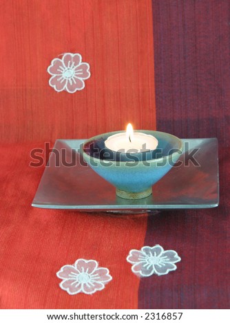Burning candle in a silver dish with white flowers