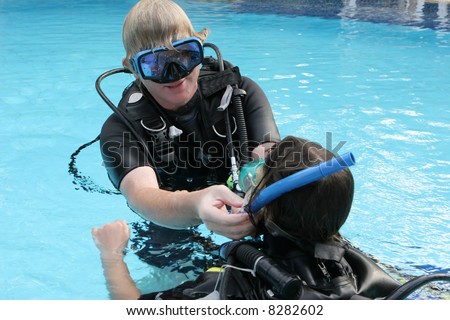 Scuba diving instructor demonstrates a skill to a student in a swimming pool.