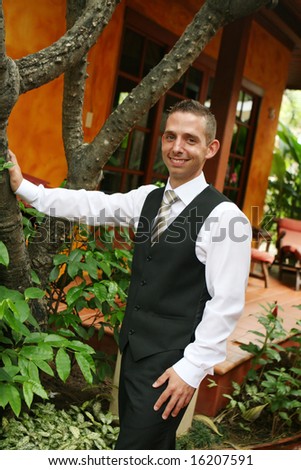 Happy young groom leaning on a tree.