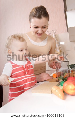Young mother preparing fresh vegetable salad with her baby daughter