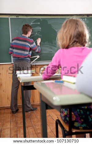 Young male teacher explaining math to the elementary age pupils at school