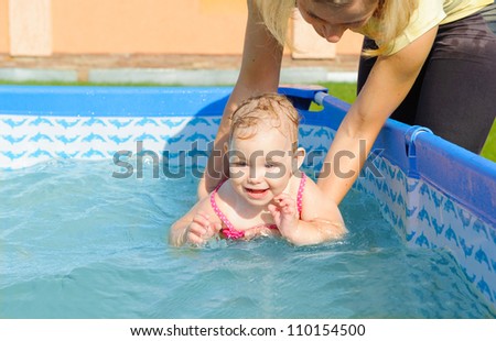 Young mother helping her daughter to swim in pool