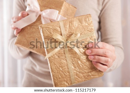 Young female holding a two boxes wrapped in golden paper with ribbon bow