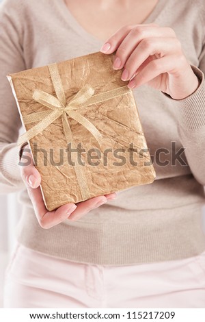 Young female holding a book wrapped in golden paper with ribbon bow
