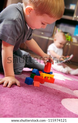 Cute kid playing with colorful cubes on the floor. His sister on background.