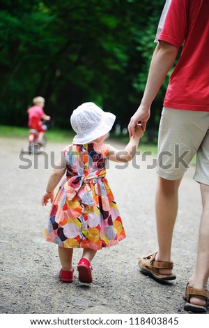Young father and his little daughter walking in the park. Little  son is riding a bicycle