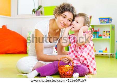 Cute little girl whispering to her mother during Easter eggs painting