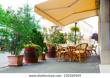 Street Cafe Under Canopy. Red Flowers In Octaves And Wood Barrels.