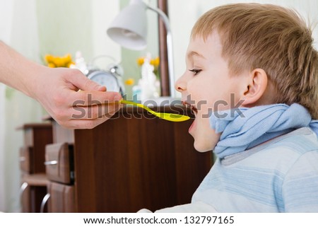 Sick boy taking medicine from spoon at home