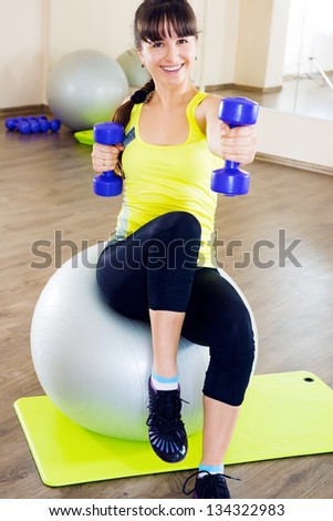 Young cheerful smiling woman exercising with dumbbells and fitball