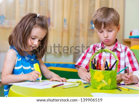 Two cute little preschool kids drawing with crayons at the table