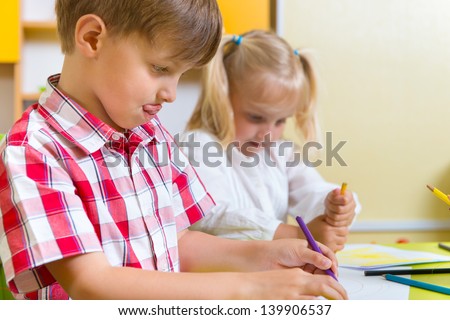 Two cute little preschool kids drawing with crayons at the table