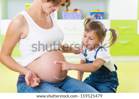 Little girl with two pigtails painting on mothers pregnant belly
