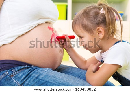 Cute little daughter painting on pregnant mother belly
