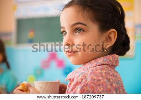 Cute little hispanic girl with cup of milk at daycare