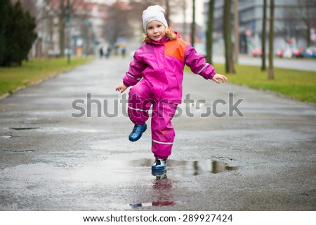 Little happy girl jumping and having fun in puddle