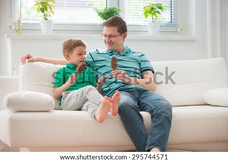 Happy father and little boy eating ice-cream on sofa