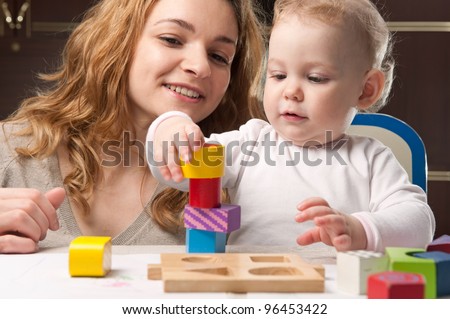 Young mother and her little baby daughter building tower with toy blocks