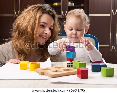 Young mother and her little baby daughter building tower with toy blocks