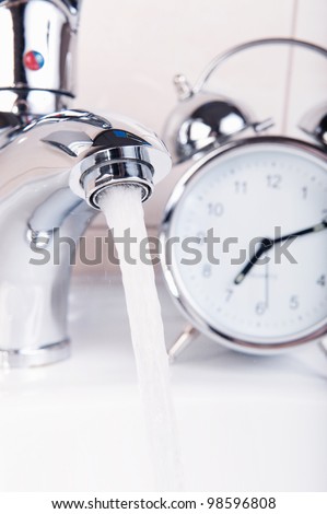 Modern chrome faucet and alarm clock. Wasting time and water concept.