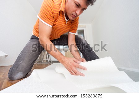 Repairs in the apartment. Man glues wallpaper in the room.