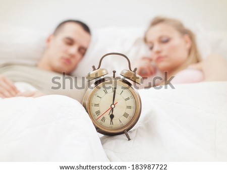 Young couple sleeping in bed. Focus on alarm clock. Intentional focus on clock