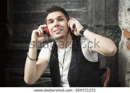 Fashionable urban young man sitting on chair in old city street listnening music.
