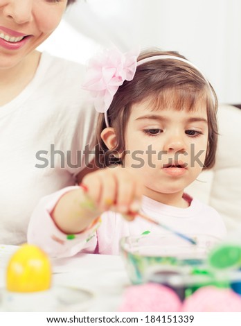 Cute little girl painting Eater eggs with her mommy. Toned image.