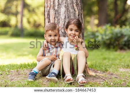 Little brother and sister expressing affection, sitting in nature and hugging.
