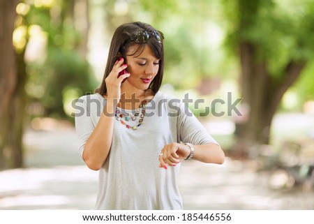 Woman checking the time and talking on the phone outdoors.