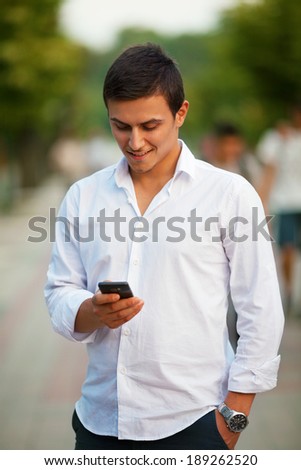 Portrait of a young man sending a message with his phone. Background is a green natural environment.