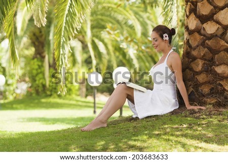 Woman reading book under palm tree on a summer day
