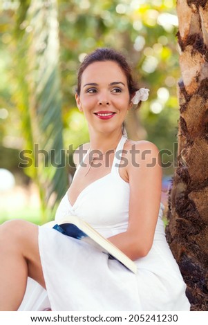 Woman reading book under palm tree