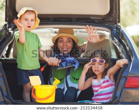 Family sitting in the back of a car smiling to camera and waving.