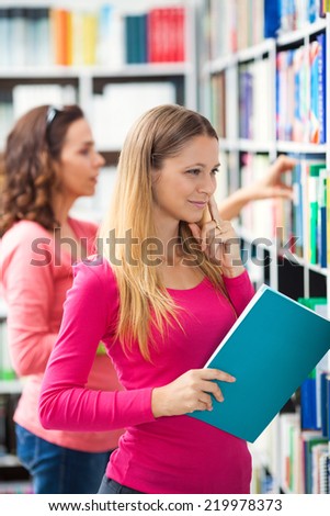 Pretty college student searching for a book in the library.